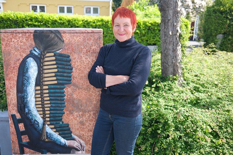 Marion Döbert steht vor einem Wandbild: Ein Mädchen hütet einen großen Stapel Bücher liebevoll im Schoß  