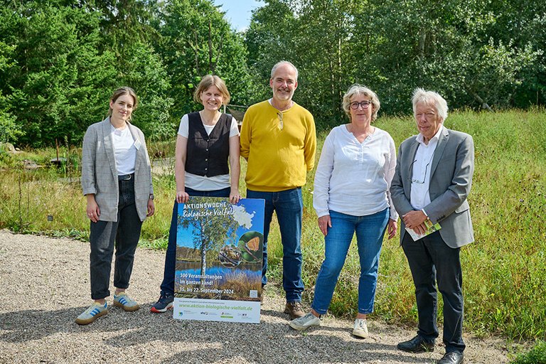 Fünf Personen stehen an einer lichten Stelle im "Arten Eden" und präsentieren das Plakat der Aktionswoche  